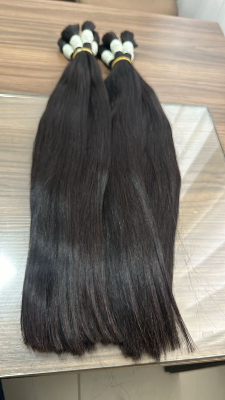 Duas mechas volumosas de mega hair preto liso apoiadas sobre uma mesa de vidro